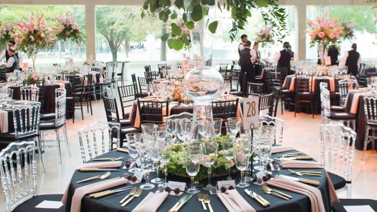 Sophistcated, elegant black and pink table scapes with round tables, oversized centerpieces in the Meyerson lobby - a group of servers gather in the back making last minute preparations
