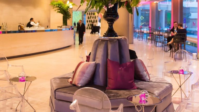 Seating area featuring circulate banquettes, flowers and ghost chairs in a romantic rosy palette